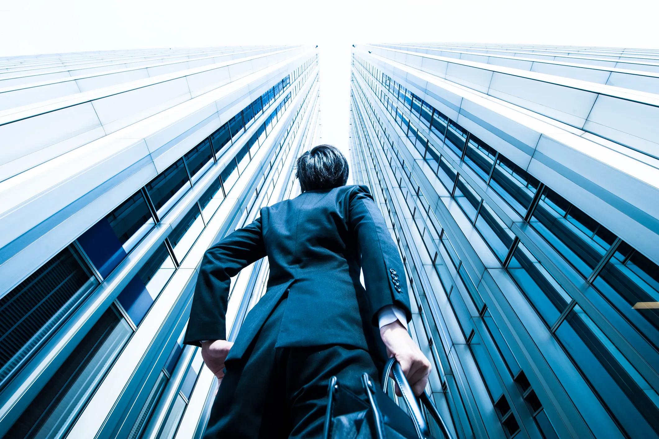 A man looks directly up at two towering buildings